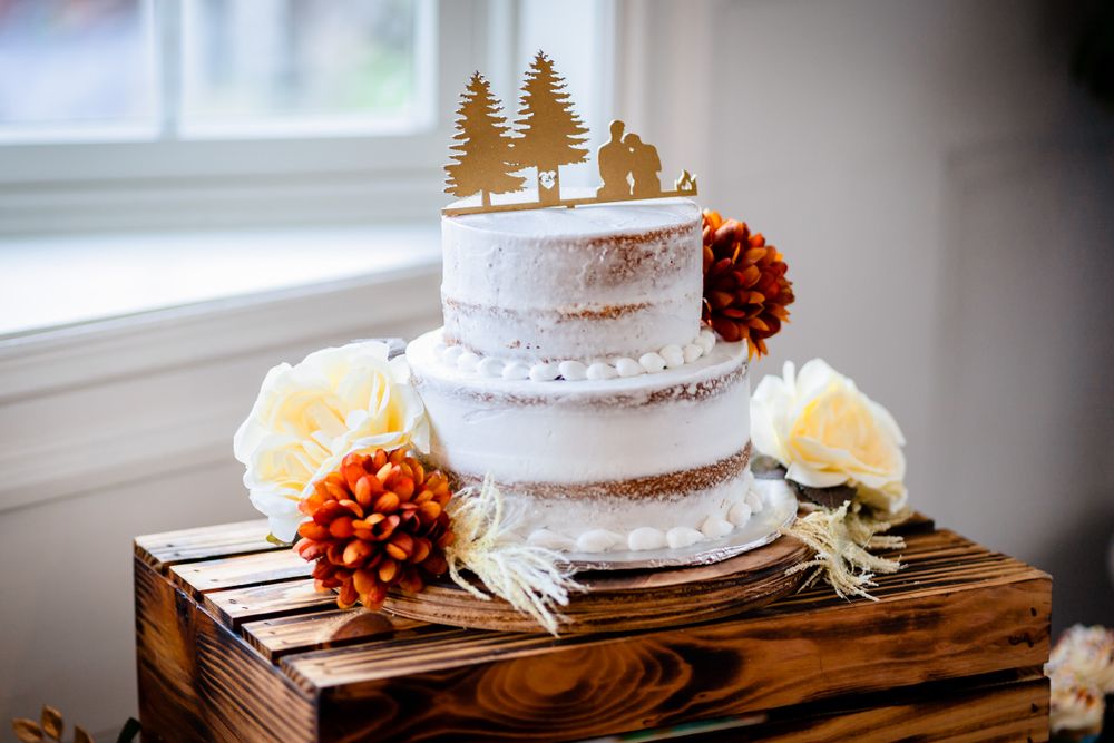 Wedding cake display with rustic wooden elements and delicate tree topper decoration.