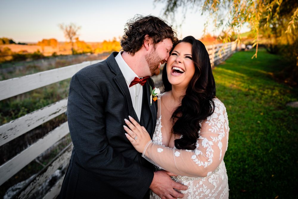 Romantic sunset wedding portrait with couple embracing near rustic wooden fence.