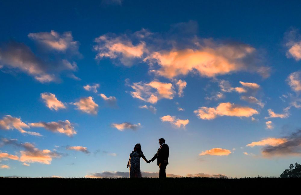 Dramatic sunset sky with pink clouds and silhouetted figures holding hands.