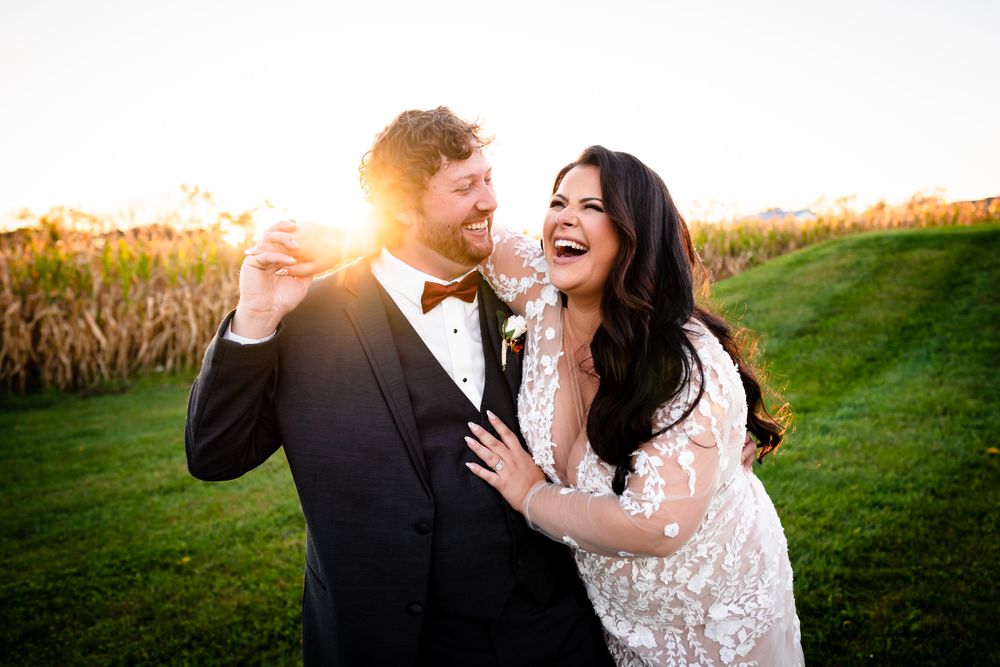 Joyful wedding couple laughing together in sunlit outdoor setting.