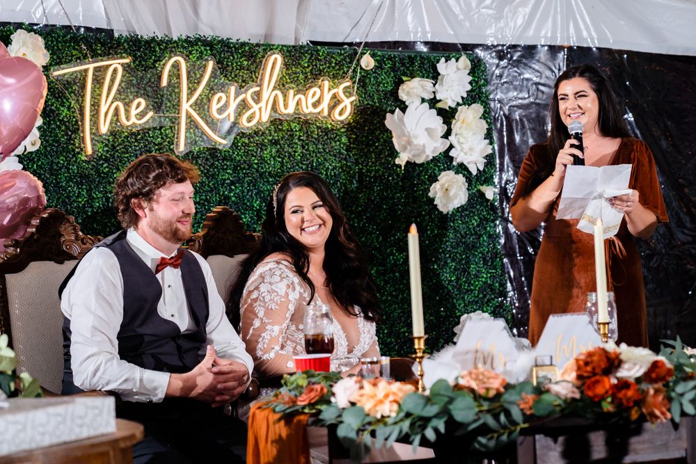 Outdoor wedding reception setup with white tents, floral decorations and a custom name sign.