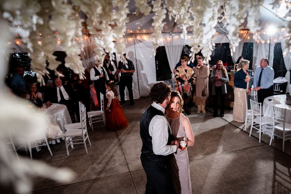 Wedding guests dancing and celebrating at an elegant reception under a white tent with string lights.