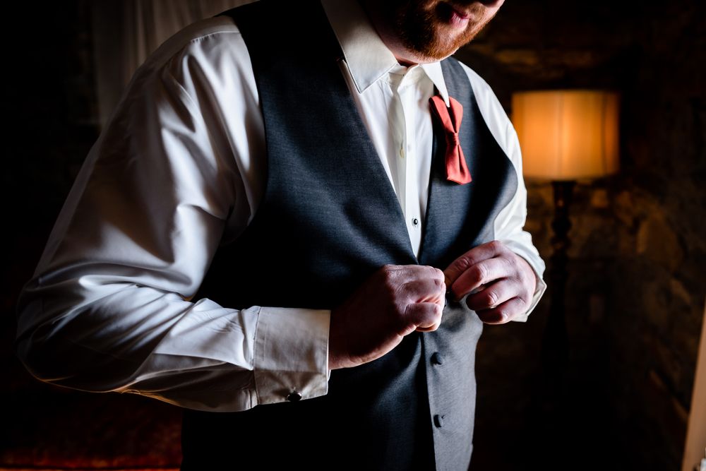 Man in formal attire preparing for event in moody lighting.