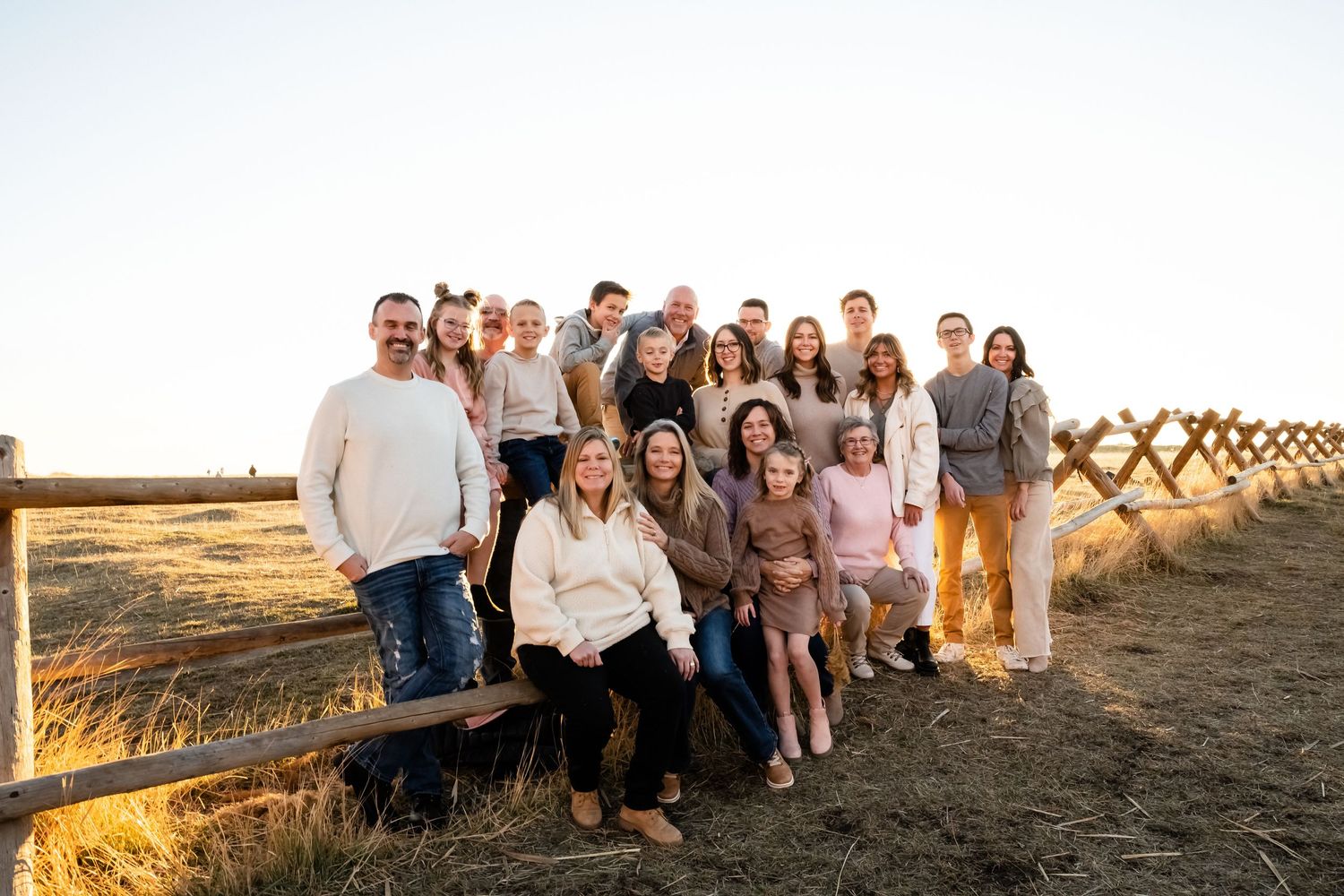 A large family group poses together on a wooden fence at sunset in a rustic outdoor setting.