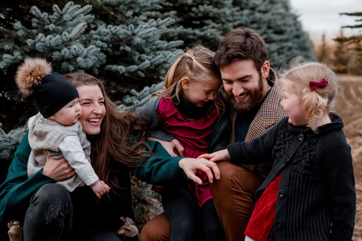 Joyful family sharing laughter together outdoors with autumn evergreens in background.