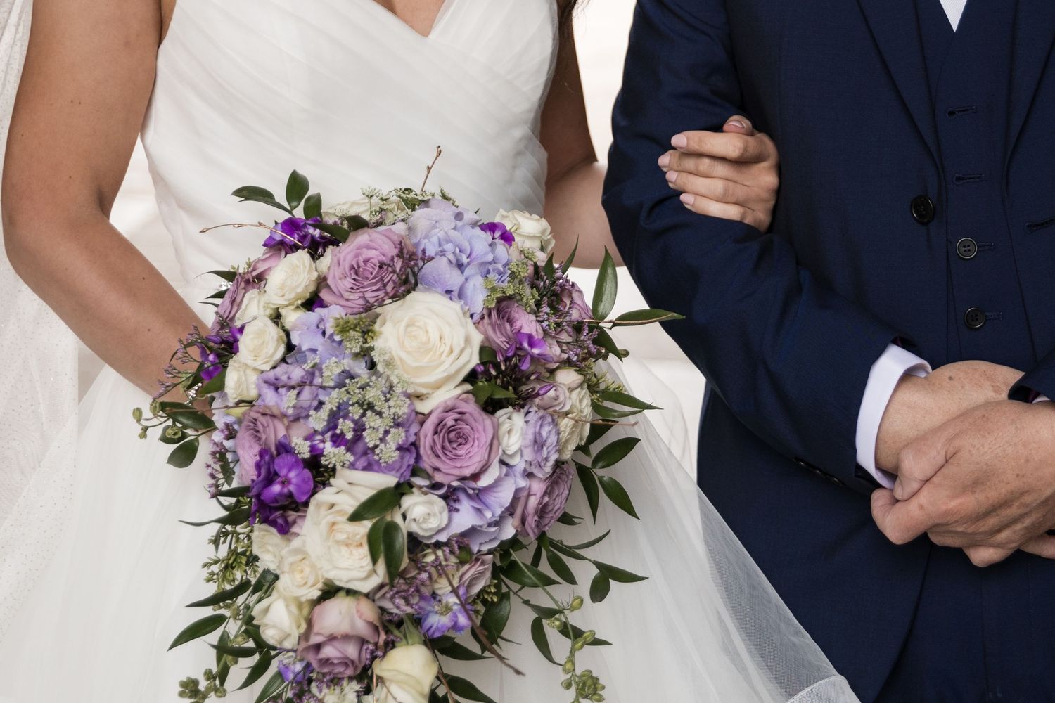 Elegant bridal bouquet features purple and white flowers with cascading greenery.