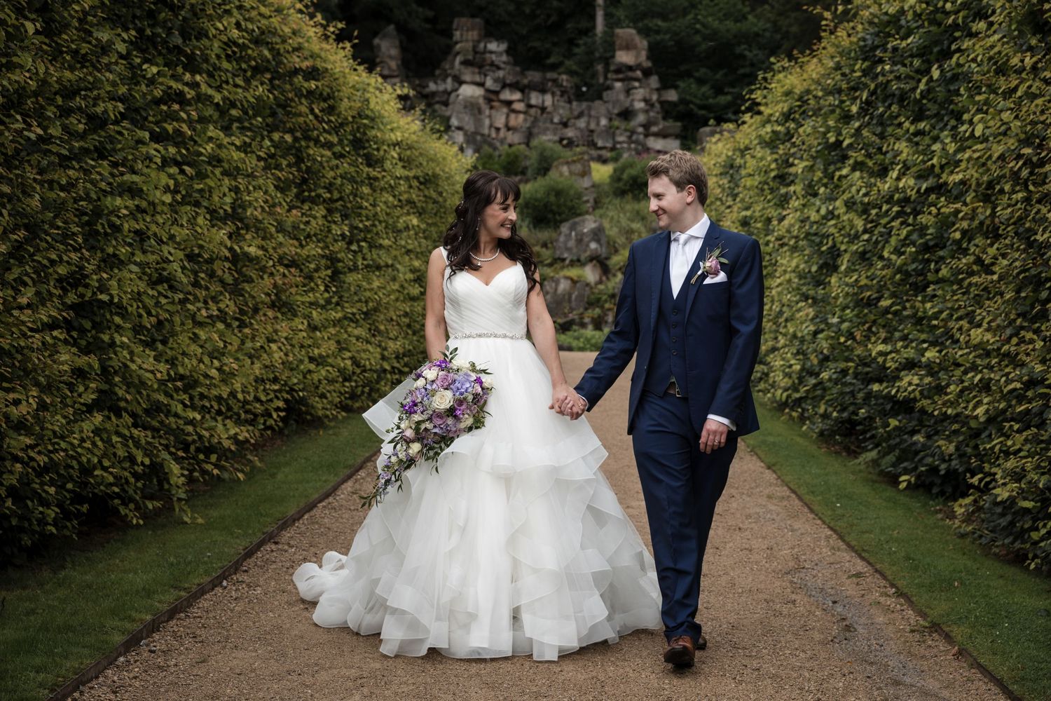 Romantic garden pathway wedding photos with lush green hedges creating natural walls.