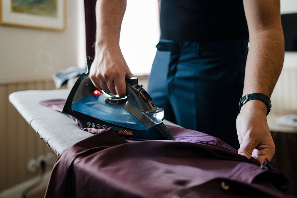 Hands pressing clothes with iron on ironing board showing cuff and watch detail.