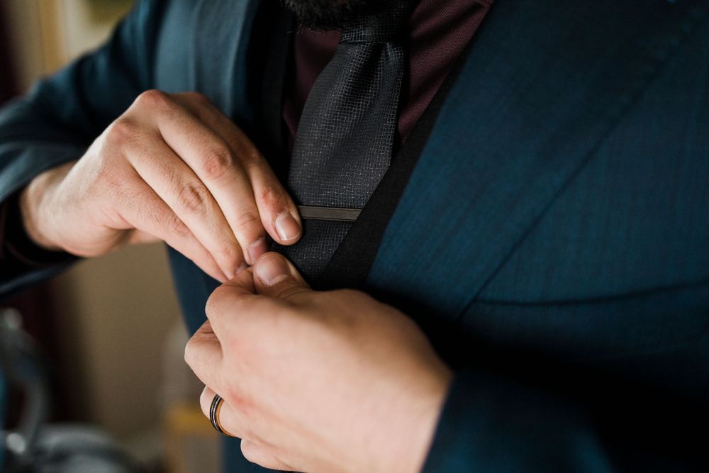 Close-up of hands adjusting a dark tie against a blue suit.