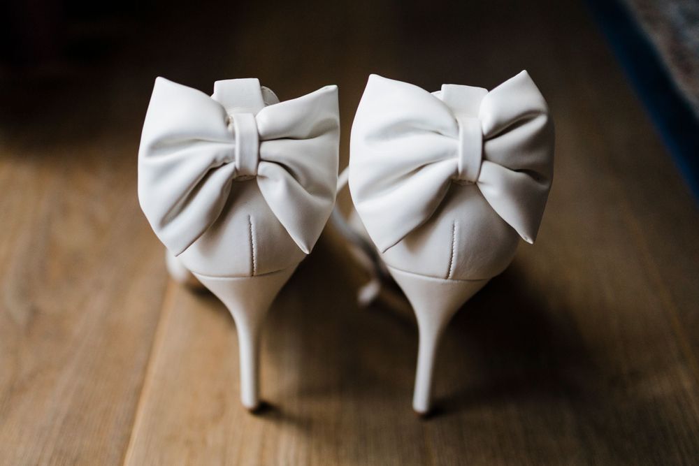 Elegant white bridal shoes with bow details on wooden floor.