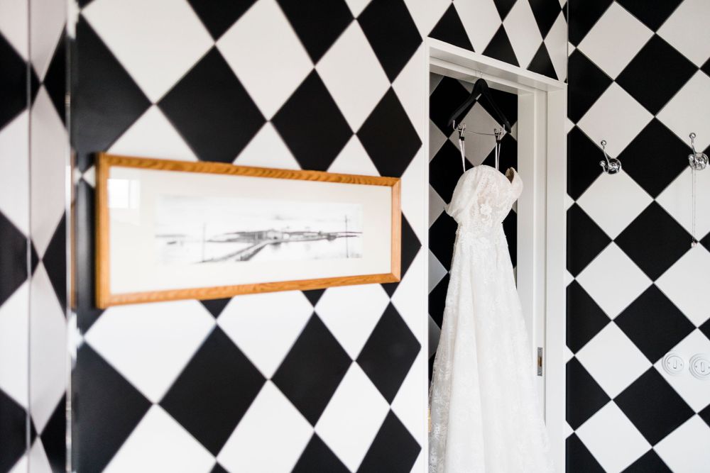 Wedding dress hanging against bold black and white diamond wallpaper in an artistic composition.