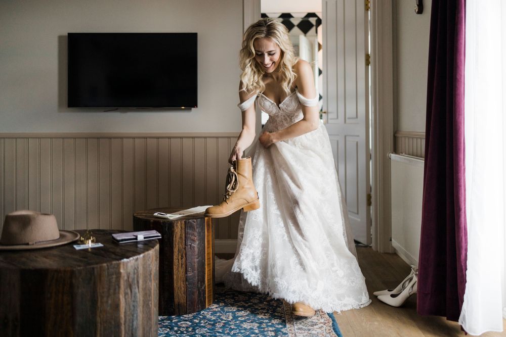 White lace wedding dress and brown boots in a room with wooden furniture and wall paneling.