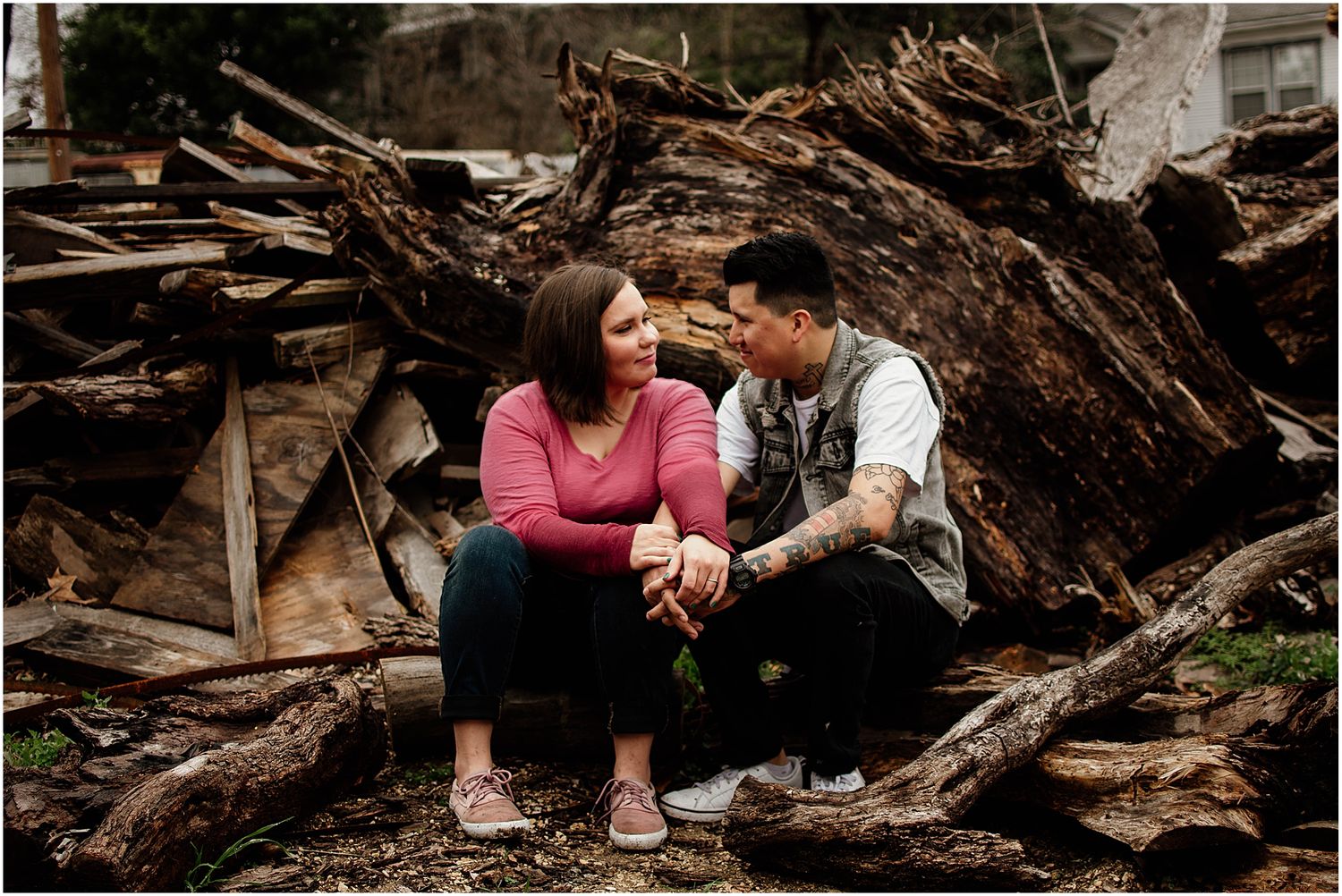 A couple shares an intimate moment while sitting on a pile of logs.