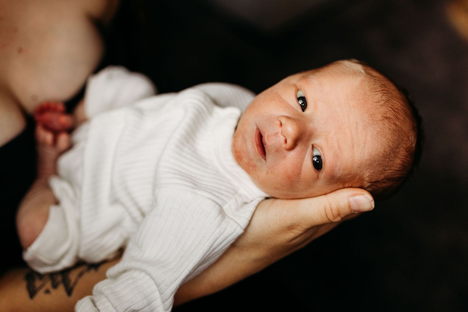 A newborn baby in white clothing lies peacefully in someone's hands.