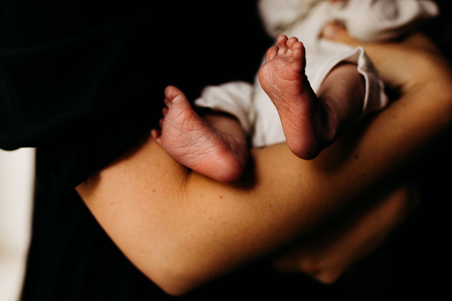 Close-up shot of tiny baby feet resting against someone's leg.