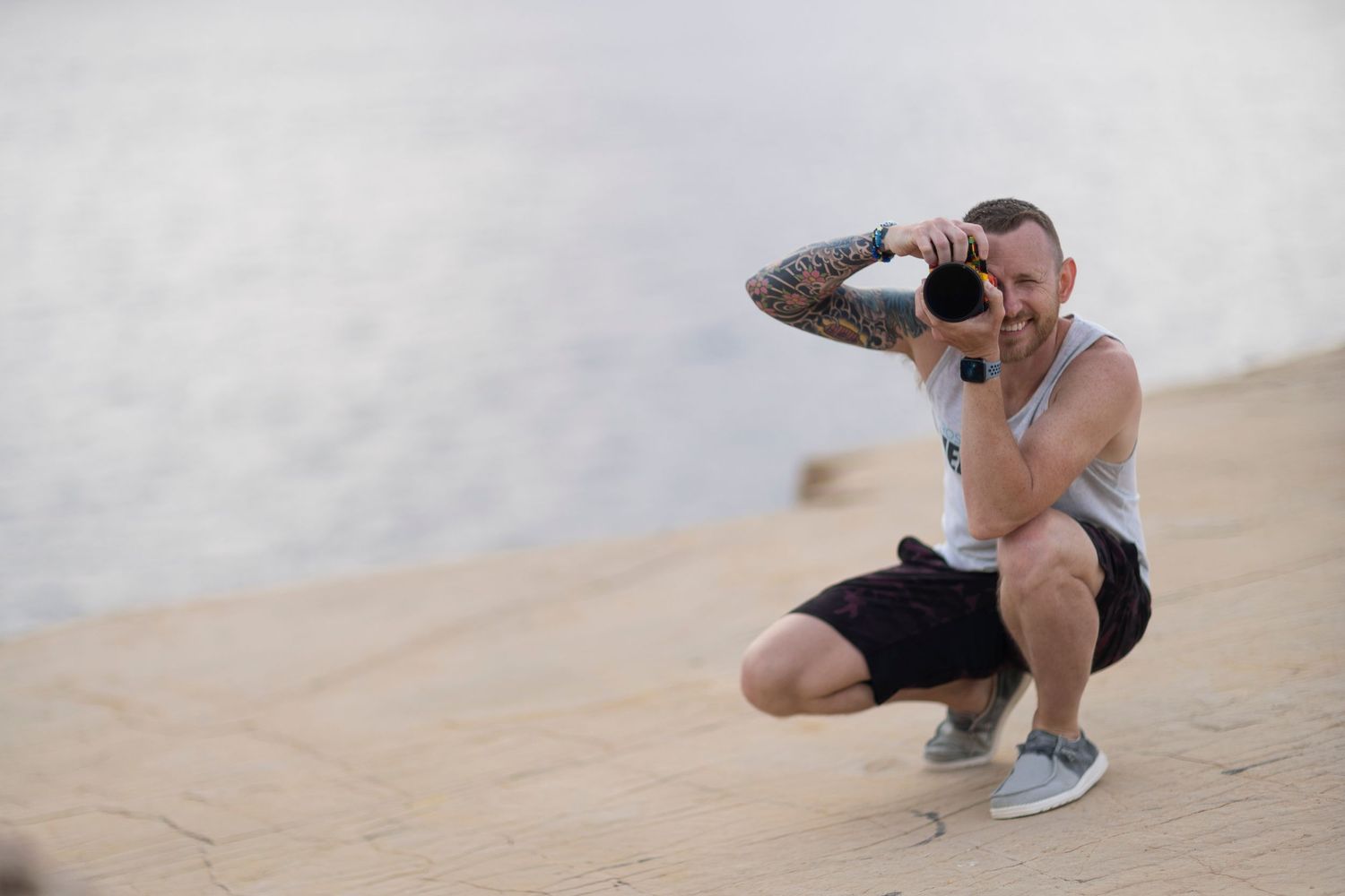 A photographer in athletic wear crouches to take a photo in a desert setting.