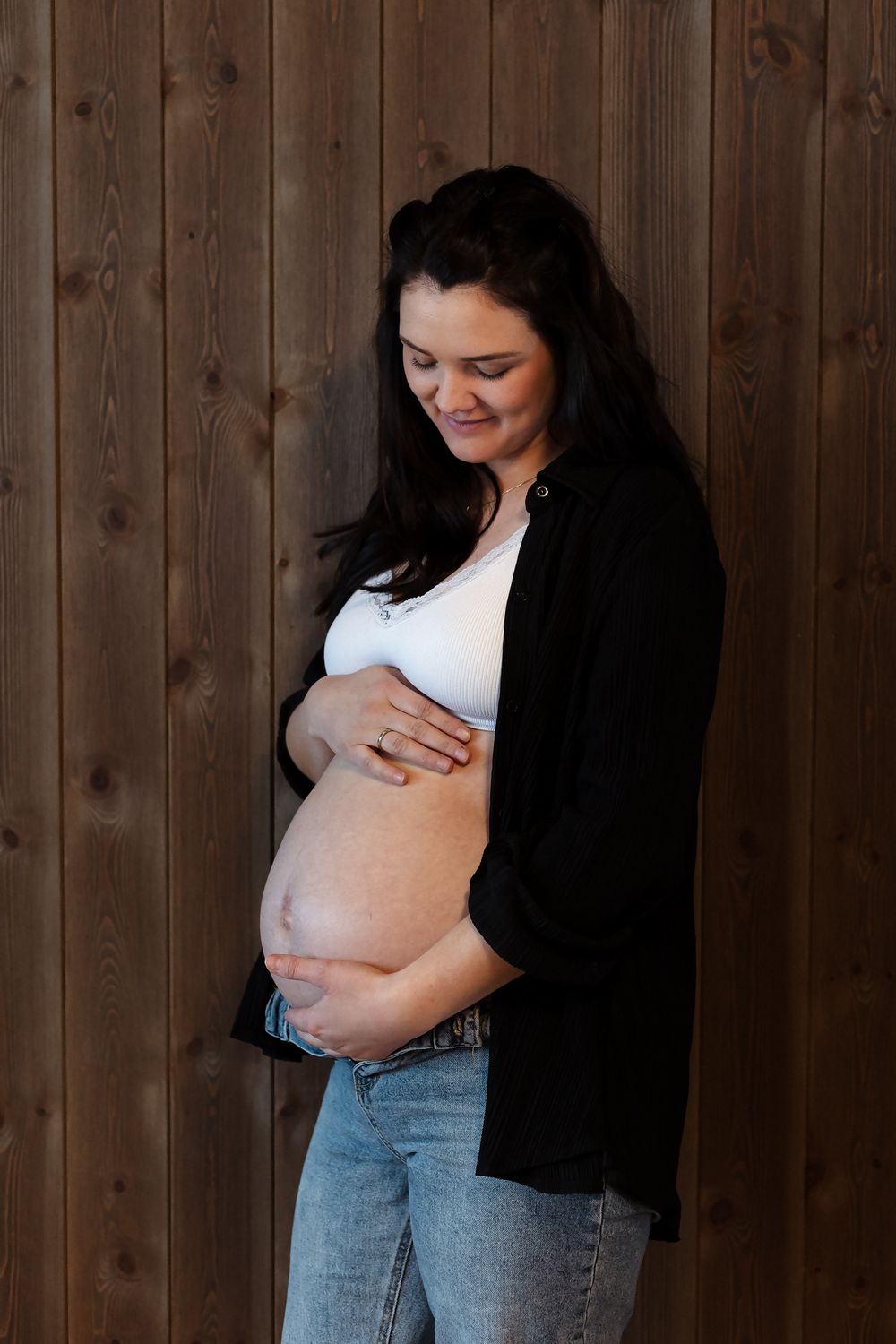 Maternity photos showing pregnant woman in casual wear against wooden backdrop.