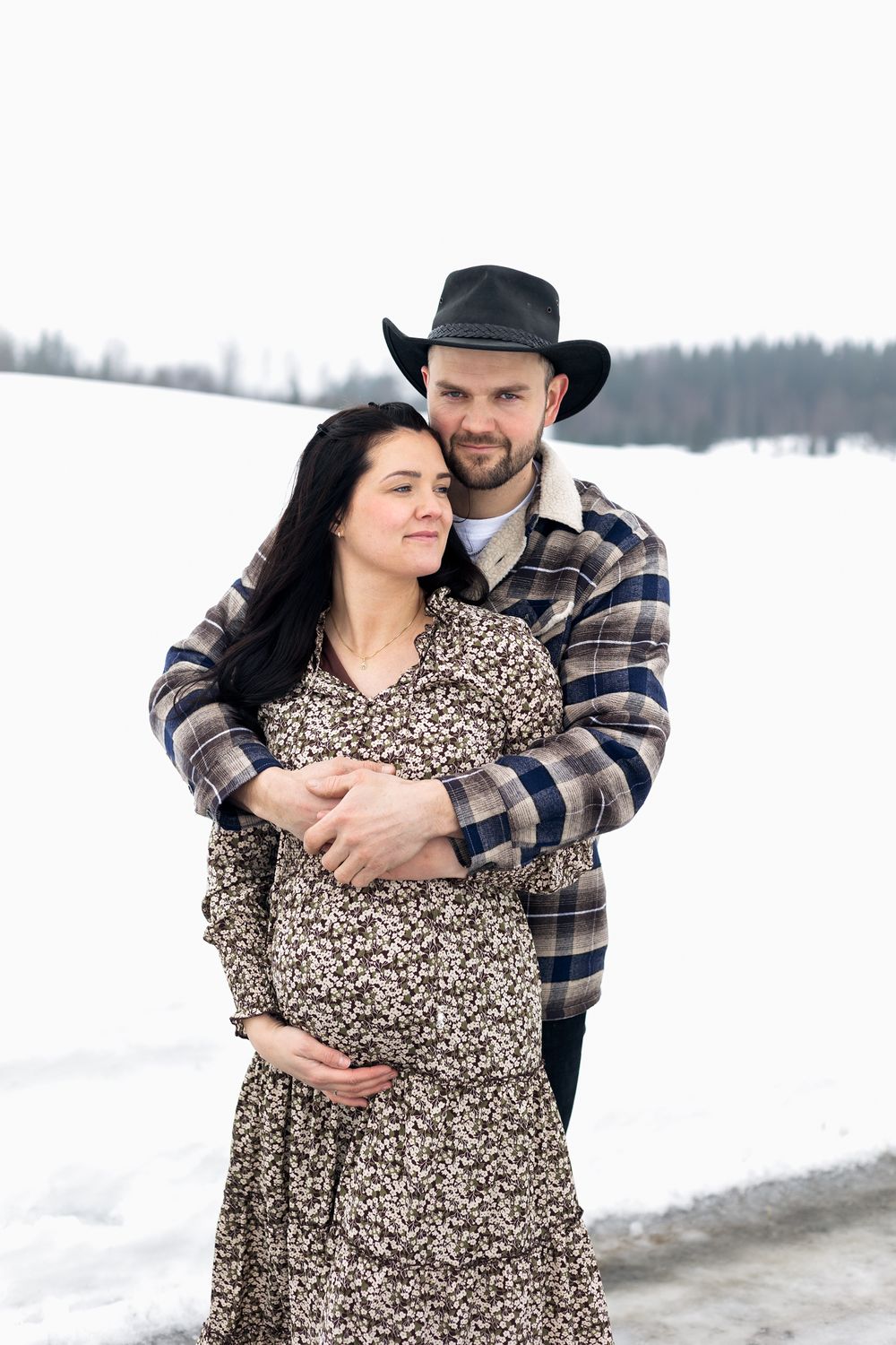 A winter maternity portrait in the snow with a snowy landscape backdrop.