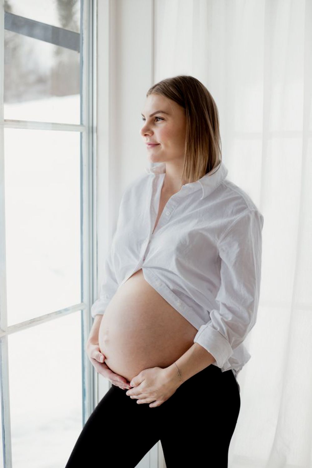 A maternity portrait by a bright window showing a pregnant belly.