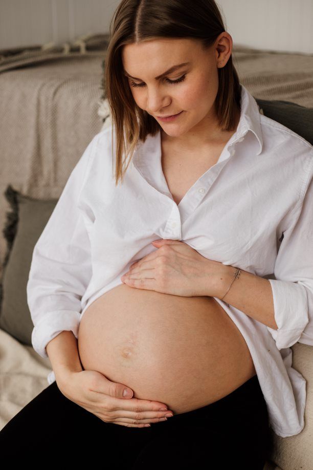 A maternity photo showing a pregnant belly in a white button-down shirt.