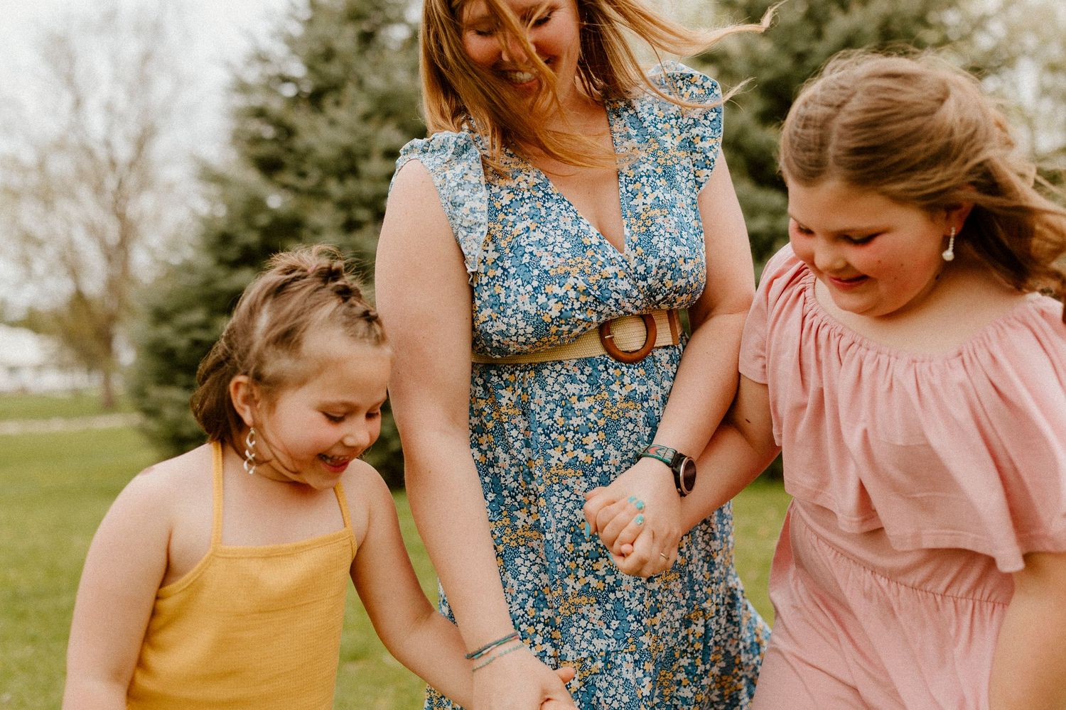 Three people in spring dresses hold hands while walking together through a sunny garden.