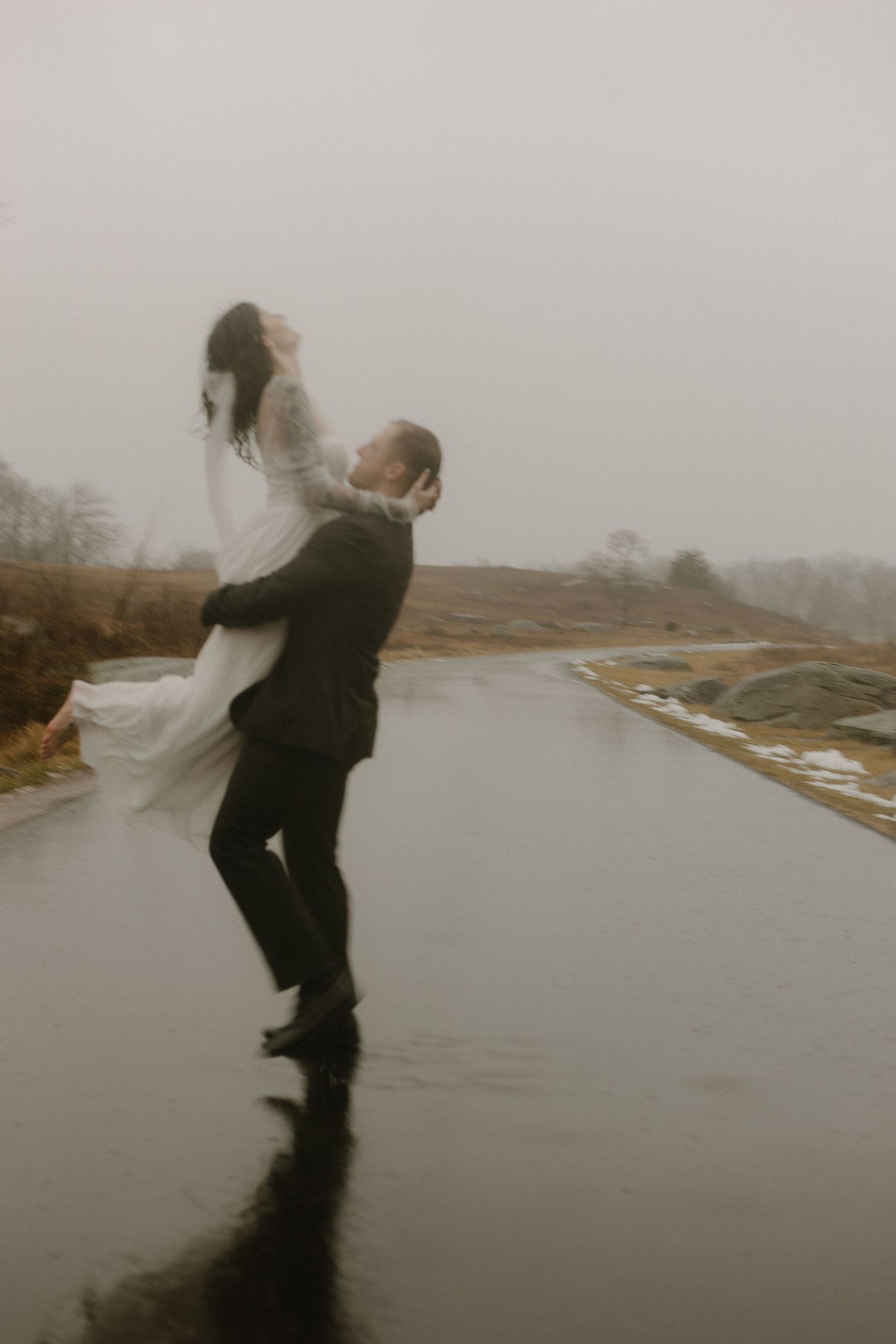 Romantic lift pose on a wet road during a misty wedding photoshoot.