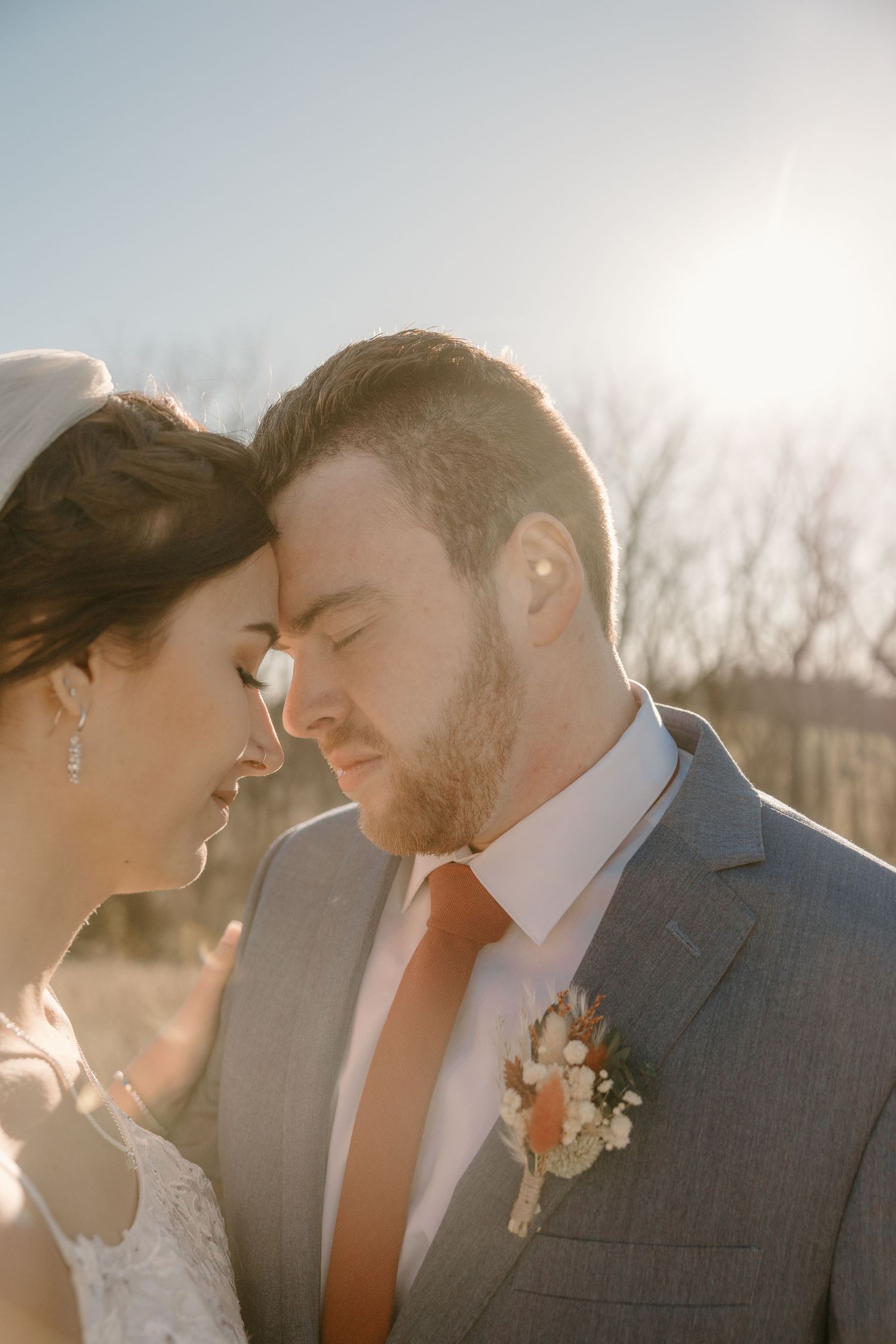 Intimate sunset wedding portrait with couple touching foreheads in golden light.