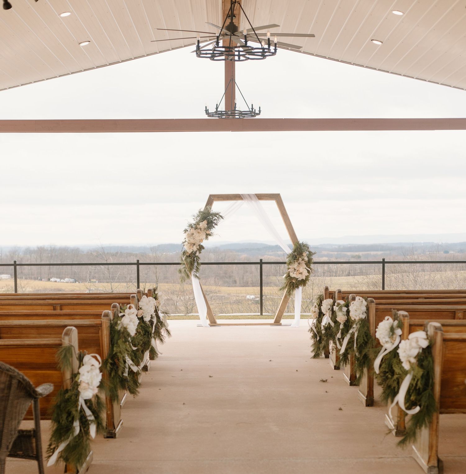 Modern chapel interior with hexagonal floral arch and decorated pews overlooking a scenic view.