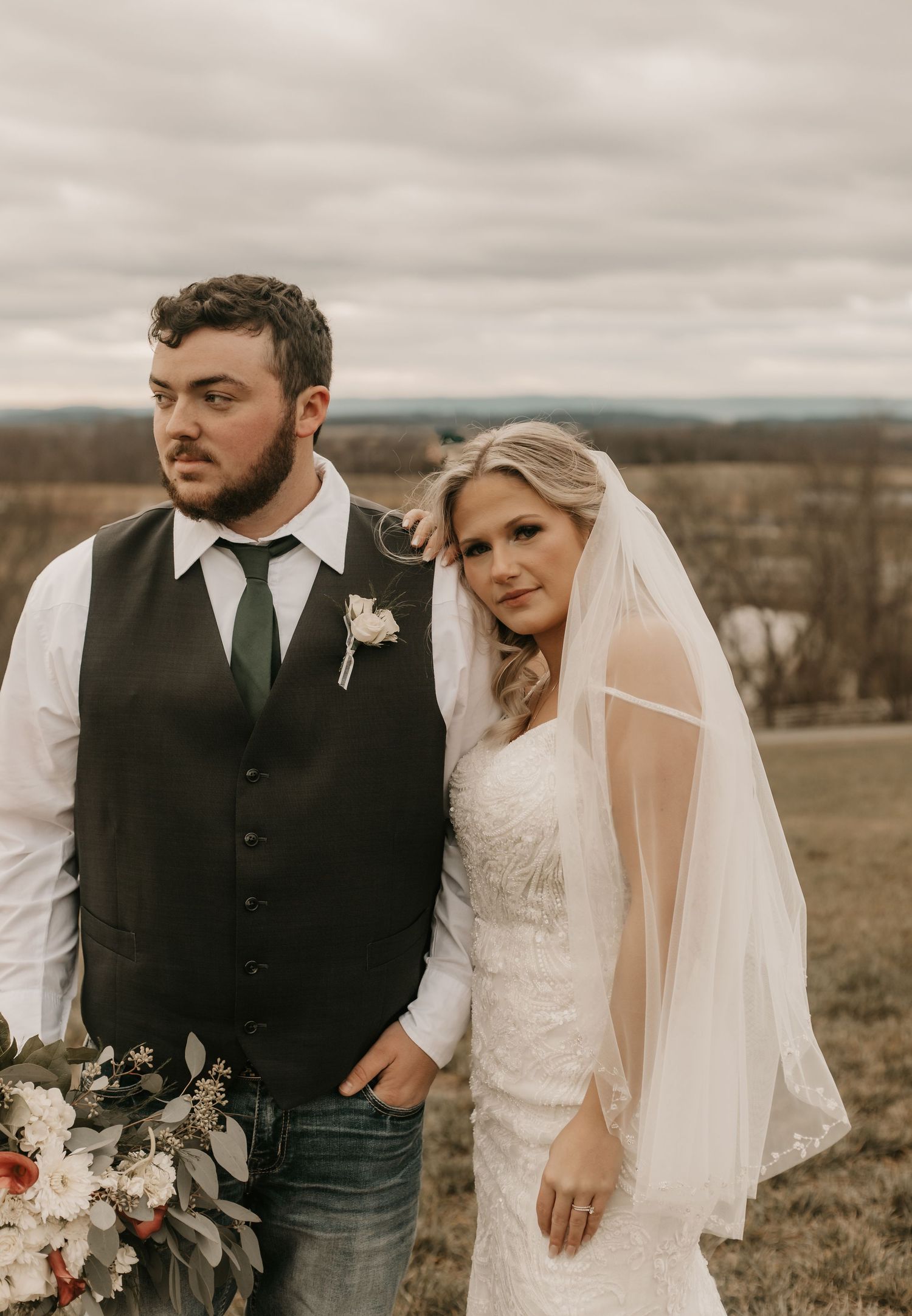 A rustic wedding portrait against an overcast rural landscape.