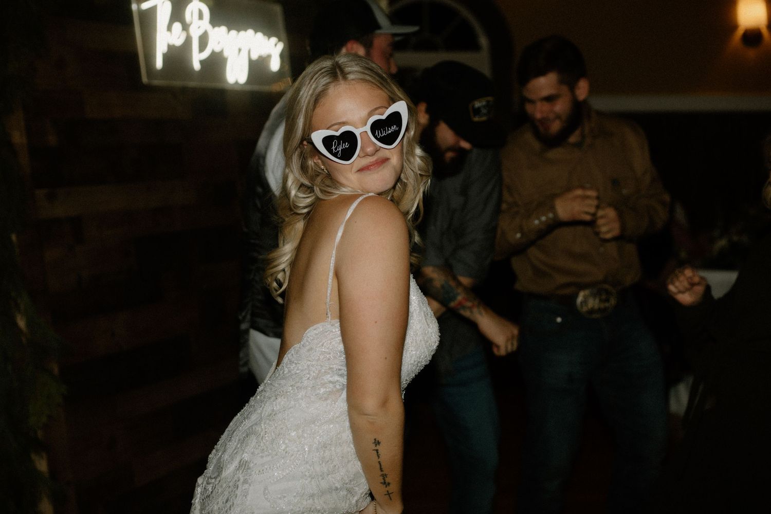 Bride wearing white retro sunglasses poses during nighttime wedding reception.