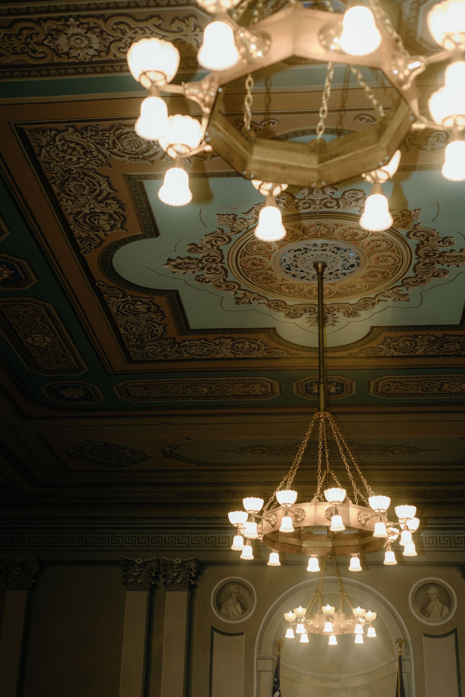 Ornate vintage chandelier hanging from an elaborately decorated ceiling with gold details.