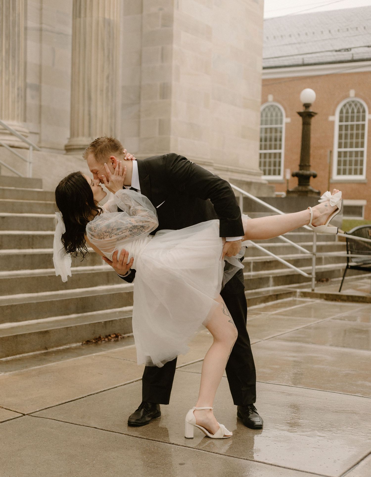 Dramatic dip pose on stone steps with bride in white dress and groom in classic black suit.