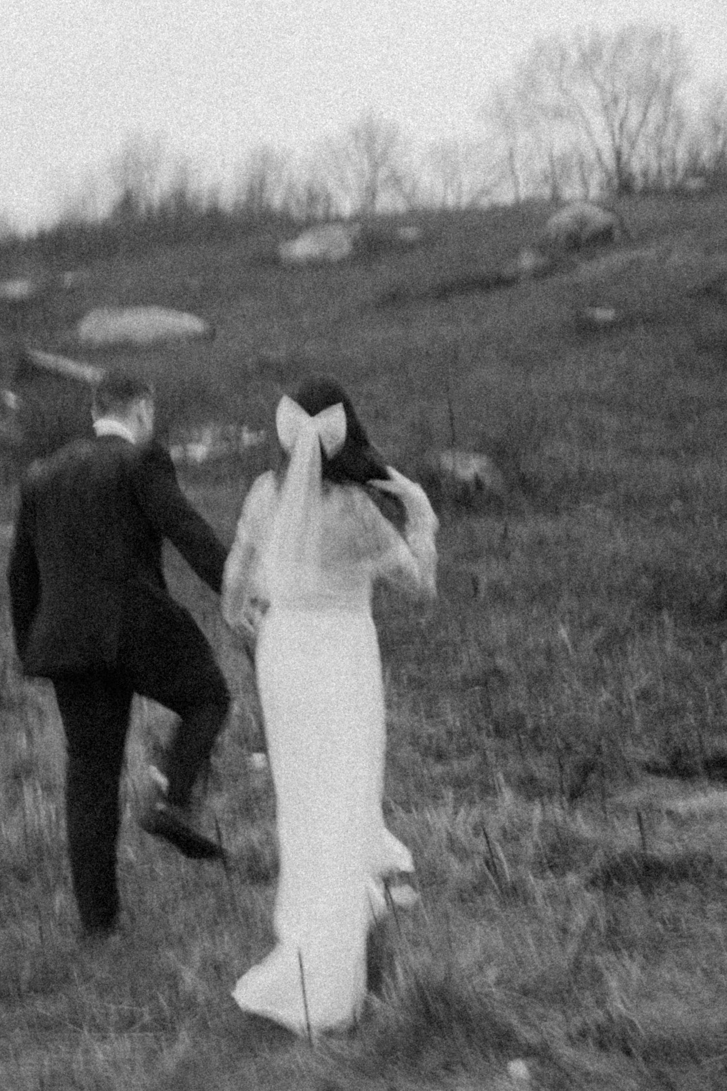 Black and white photo of a couple walking up a hill in wedding attire.