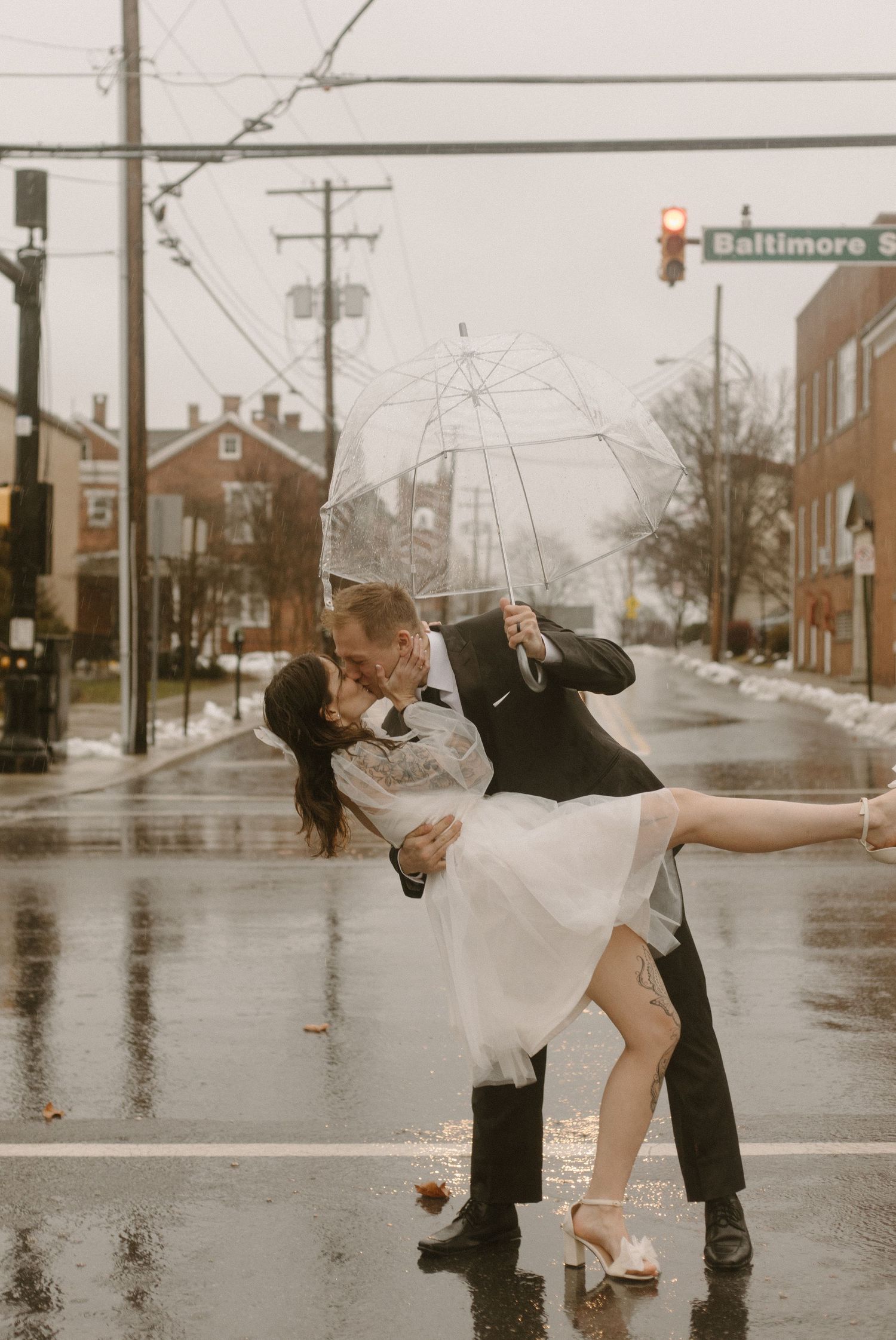 A couple dances in the rain on a wet city street with an umbrella.