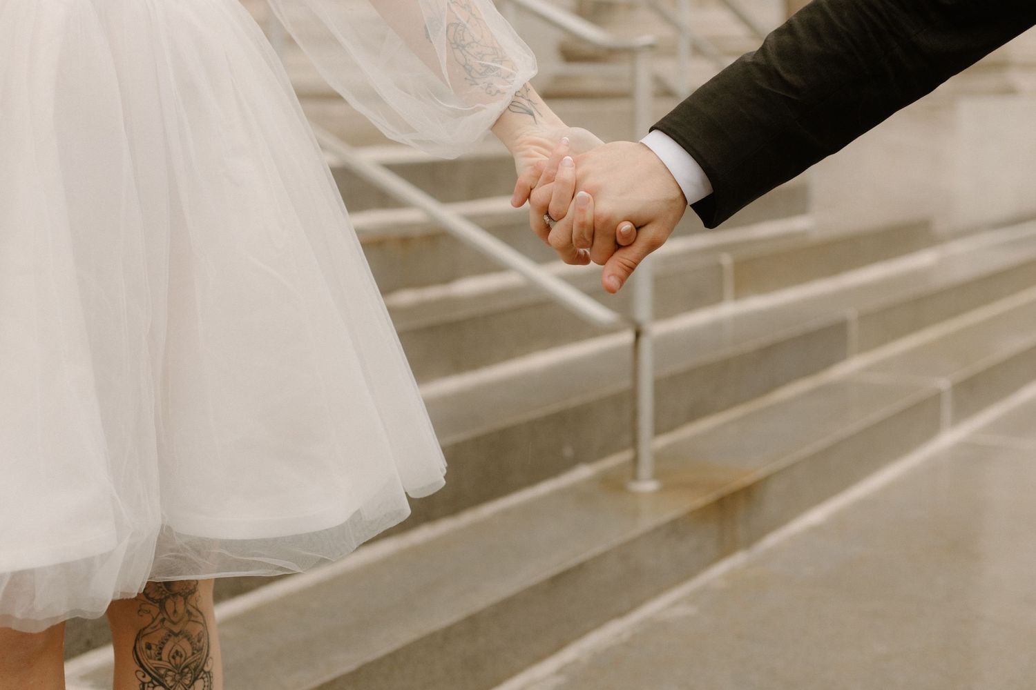 Close-up of couple holding hands while walking up concrete stairs, showing their formal wedding attire.