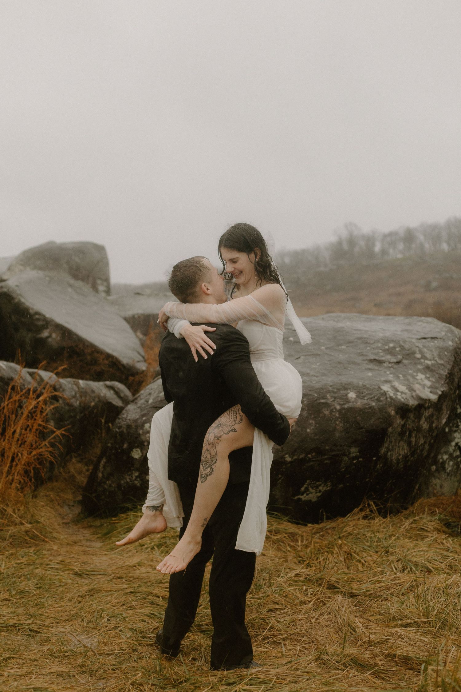 A playful wedding photo of a couple by rocky terrain, with one person being lifted up.