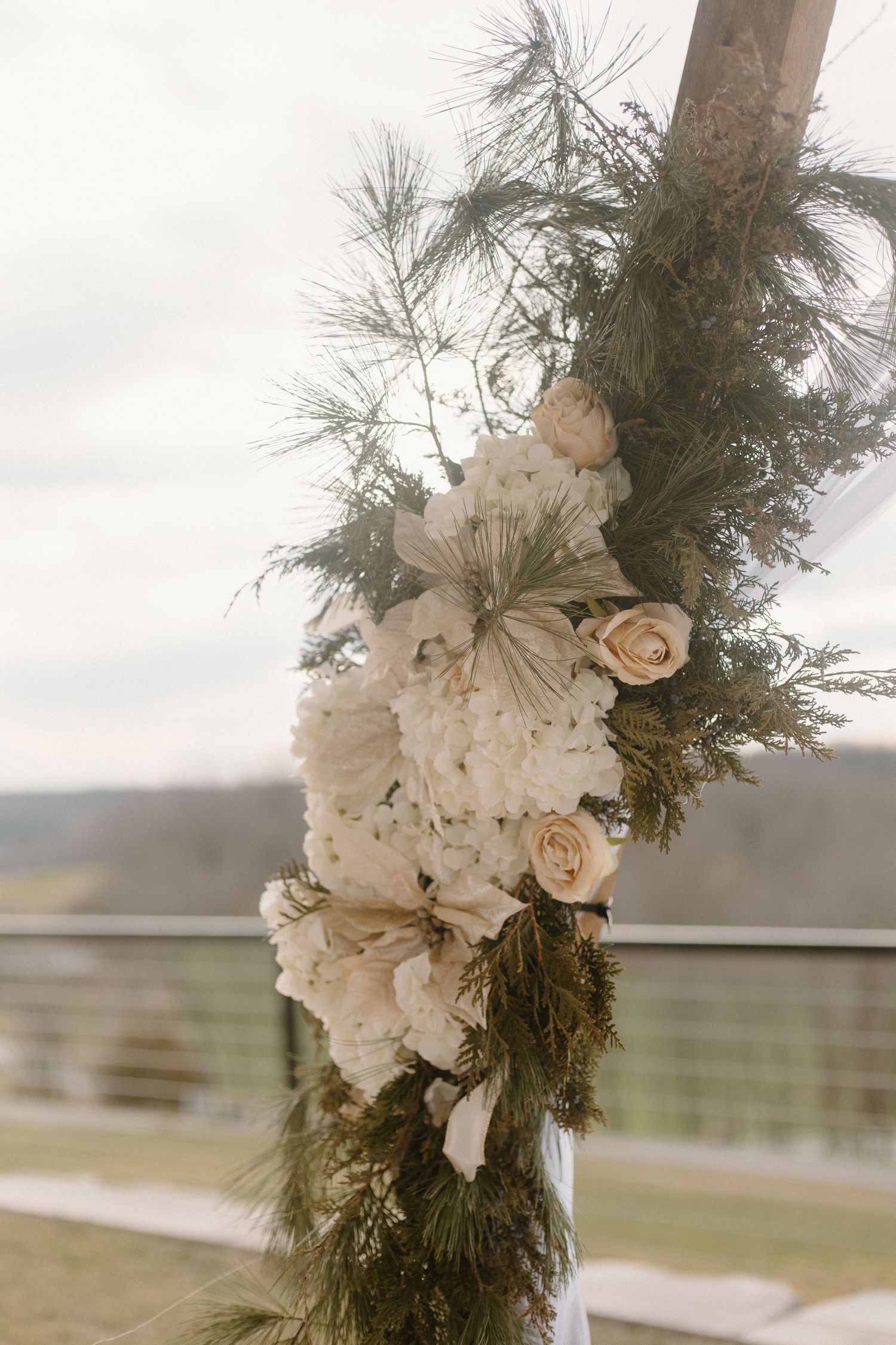 Elegant floral arrangement with white roses and greenery wrapped around a wooden post.