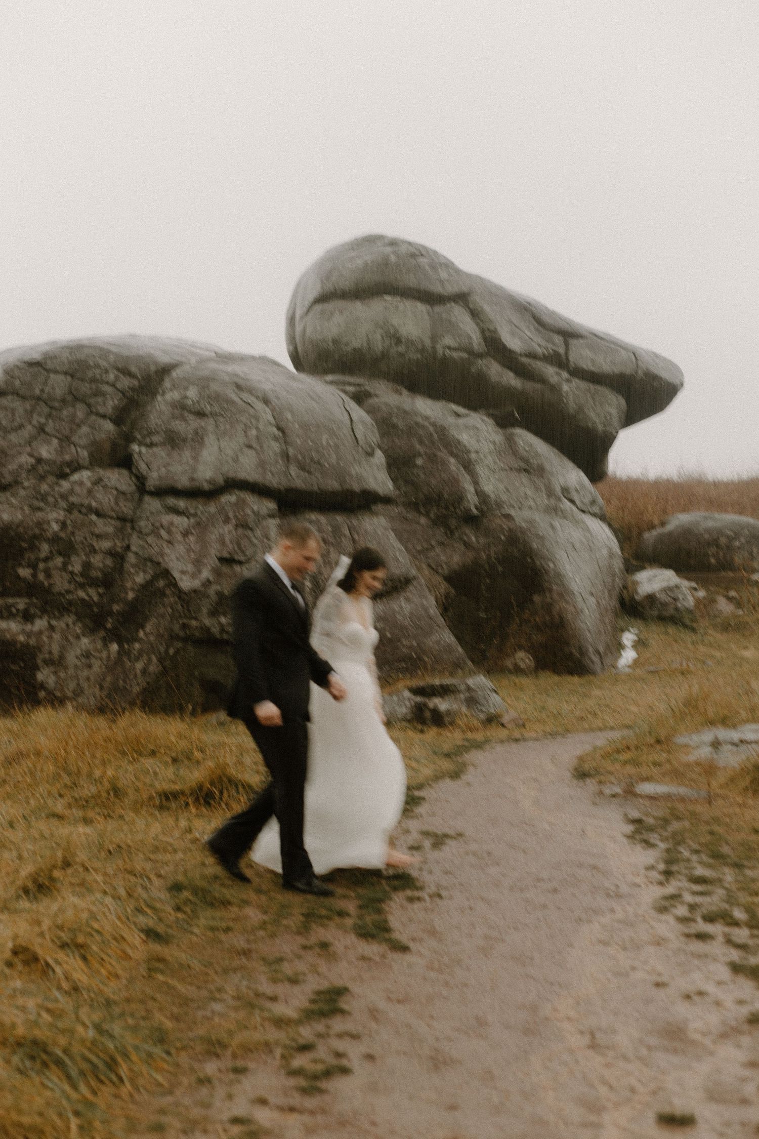 A couple walking along a path beside massive rock formations on their wedding day.