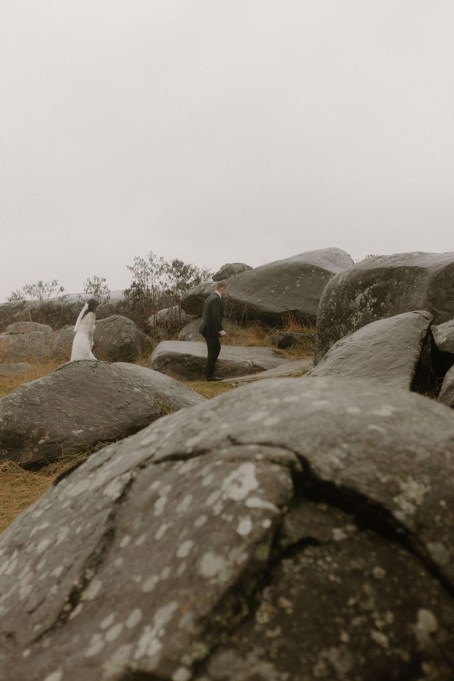An artistic wide-angle shot of a couple amid large rock formations, photographed from a low perspective.