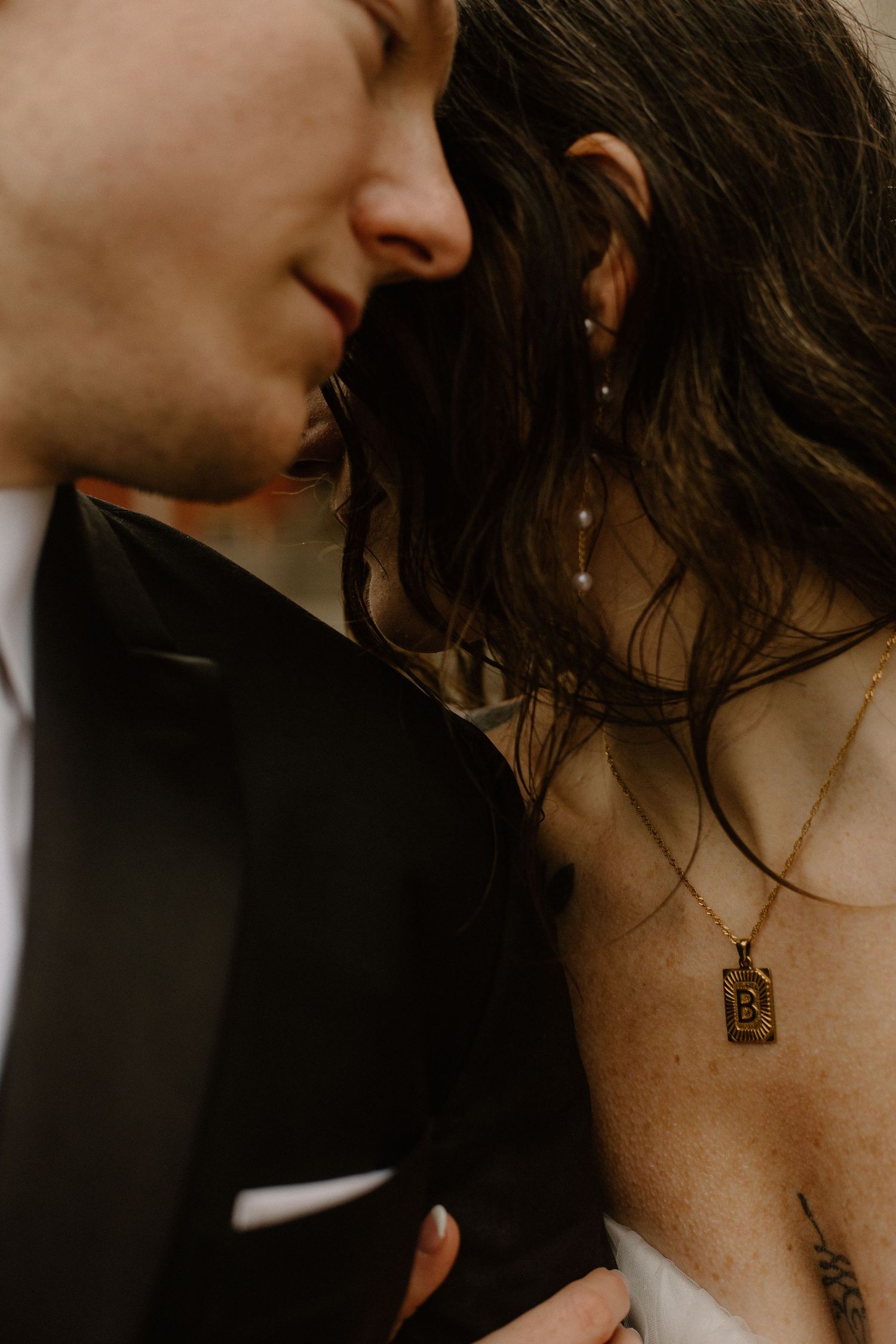 Warm-toned close-up showing jewelry detail and intimate moment between wedding couple.