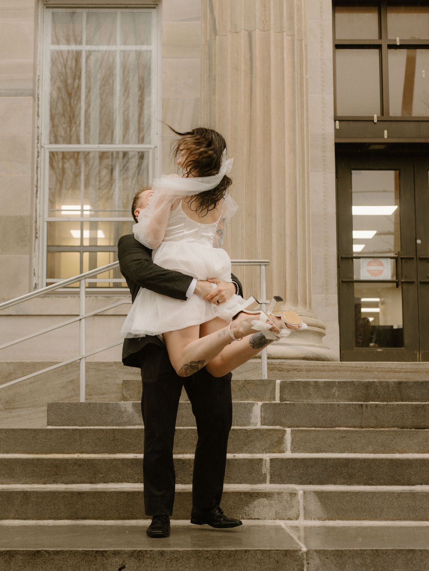 A romantic lift pose on building steps during a rainy photoshoot.