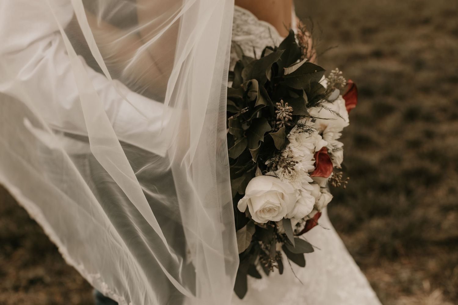 Close-up of flowing white wedding veil and bridal bouquet with mixed flowers.