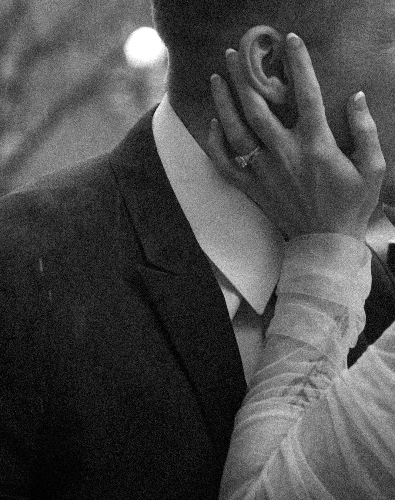 A tender moment captured in black and white as hands touch during a formal occasion.