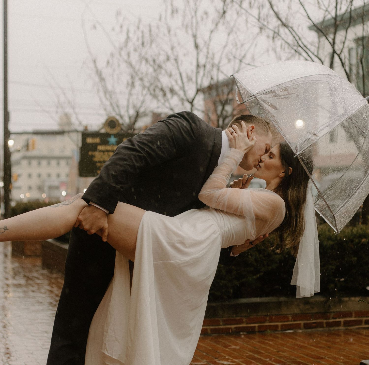 A couple sharing a romantic dip kiss under an umbrella in the rain.