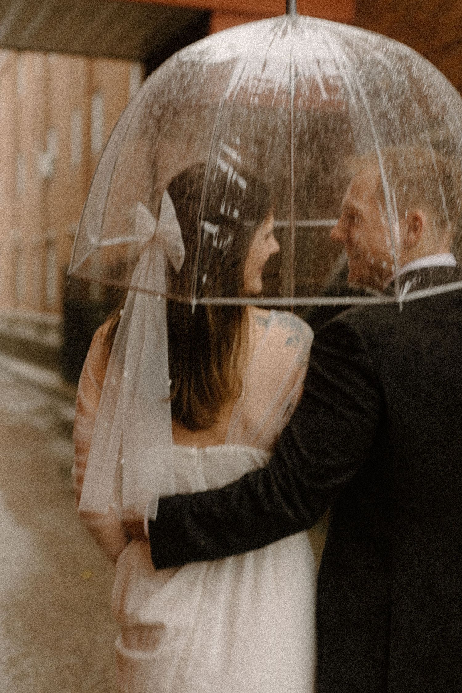 A romantic couple shares an intimate moment under a clear umbrella on a rainy day.