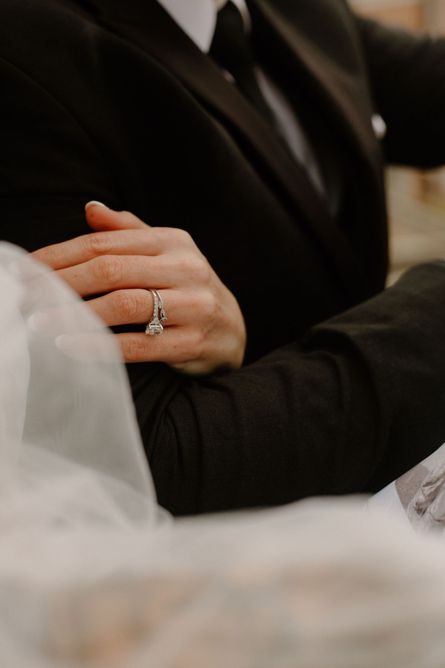Close-up detail of hands with engagement ring against formal attire.