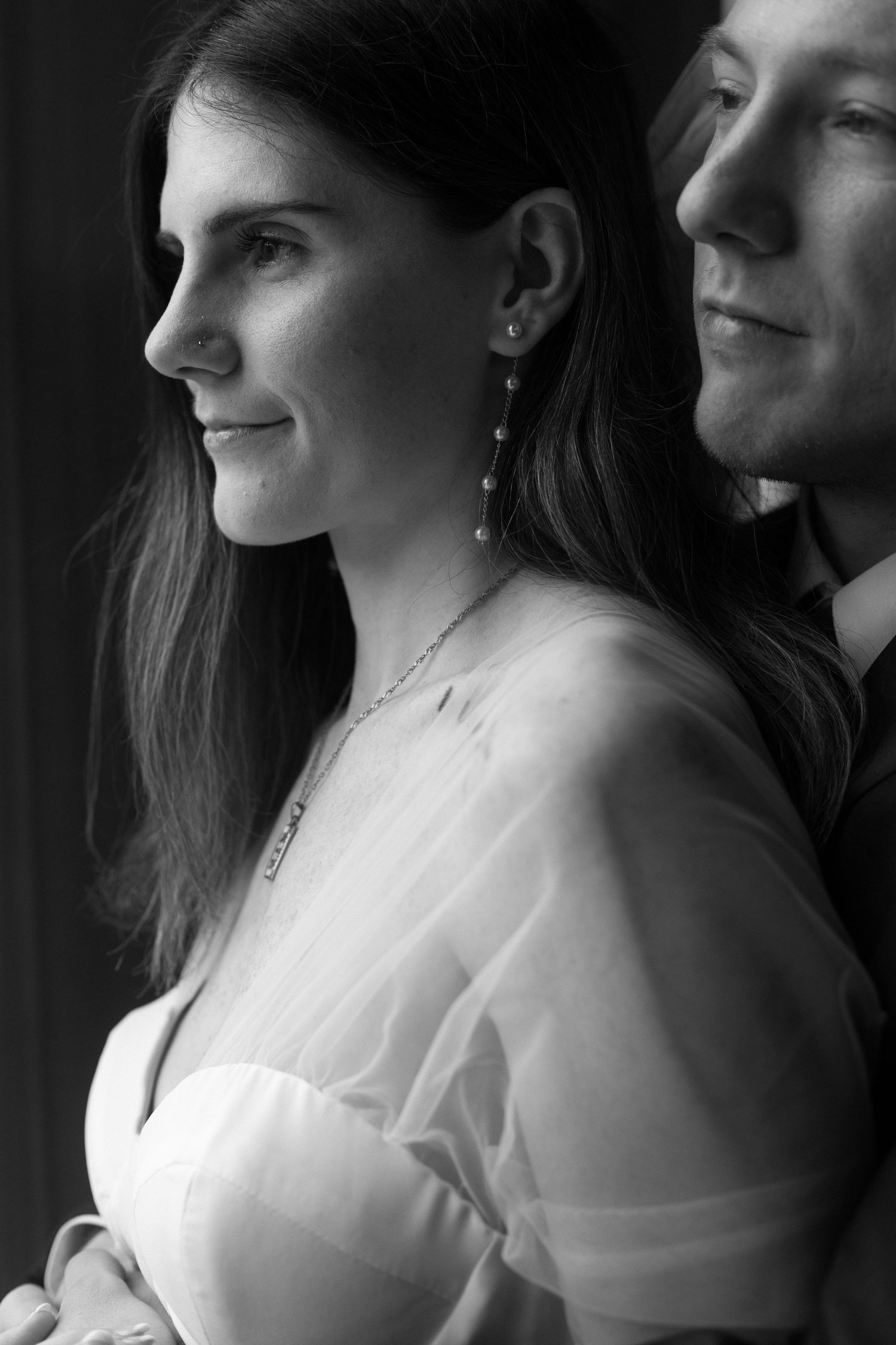 A romantic black and white portrait of a couple by a window.