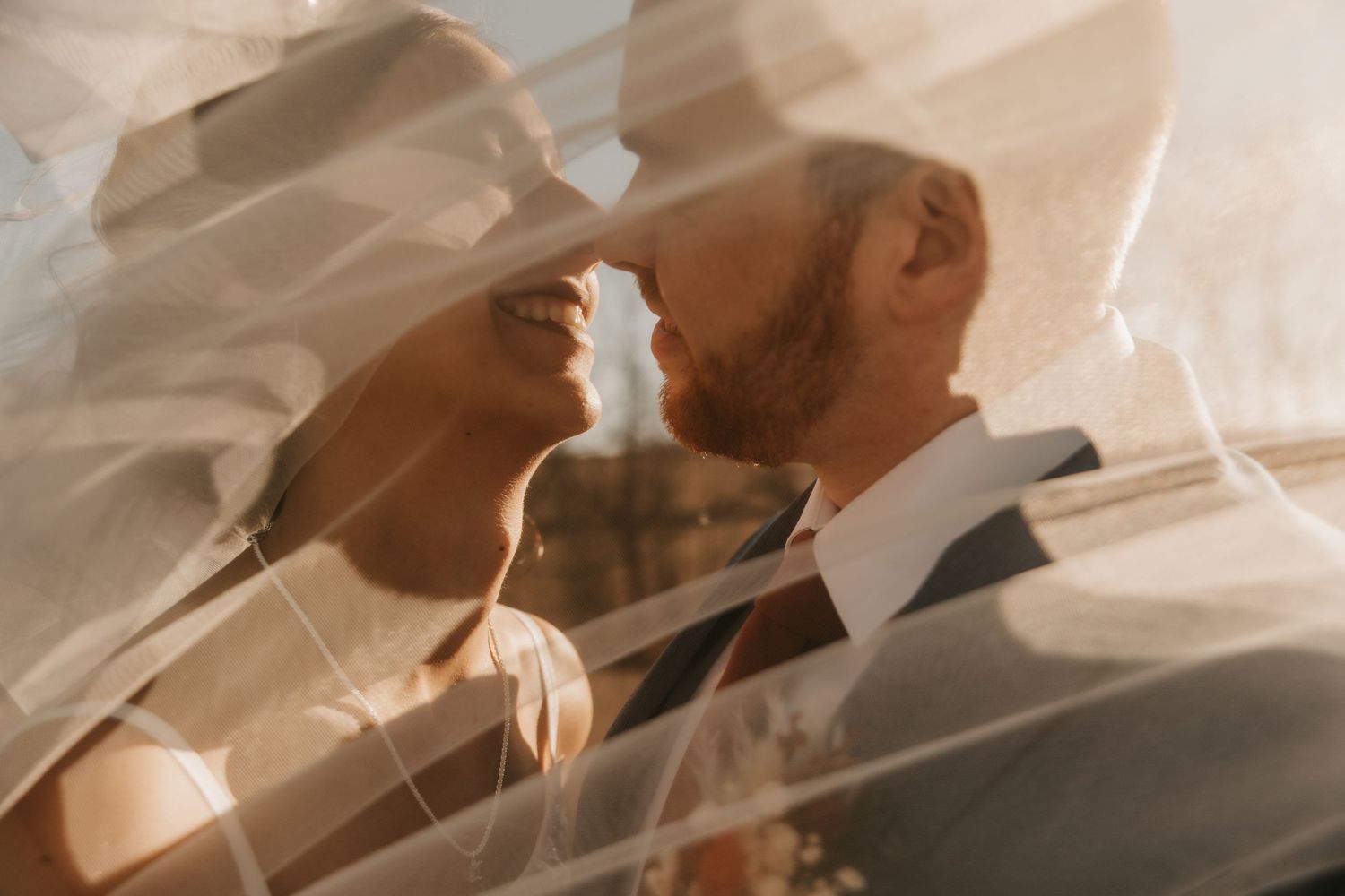 Artistic veiled wedding portrait showing couple in close intimate moment.