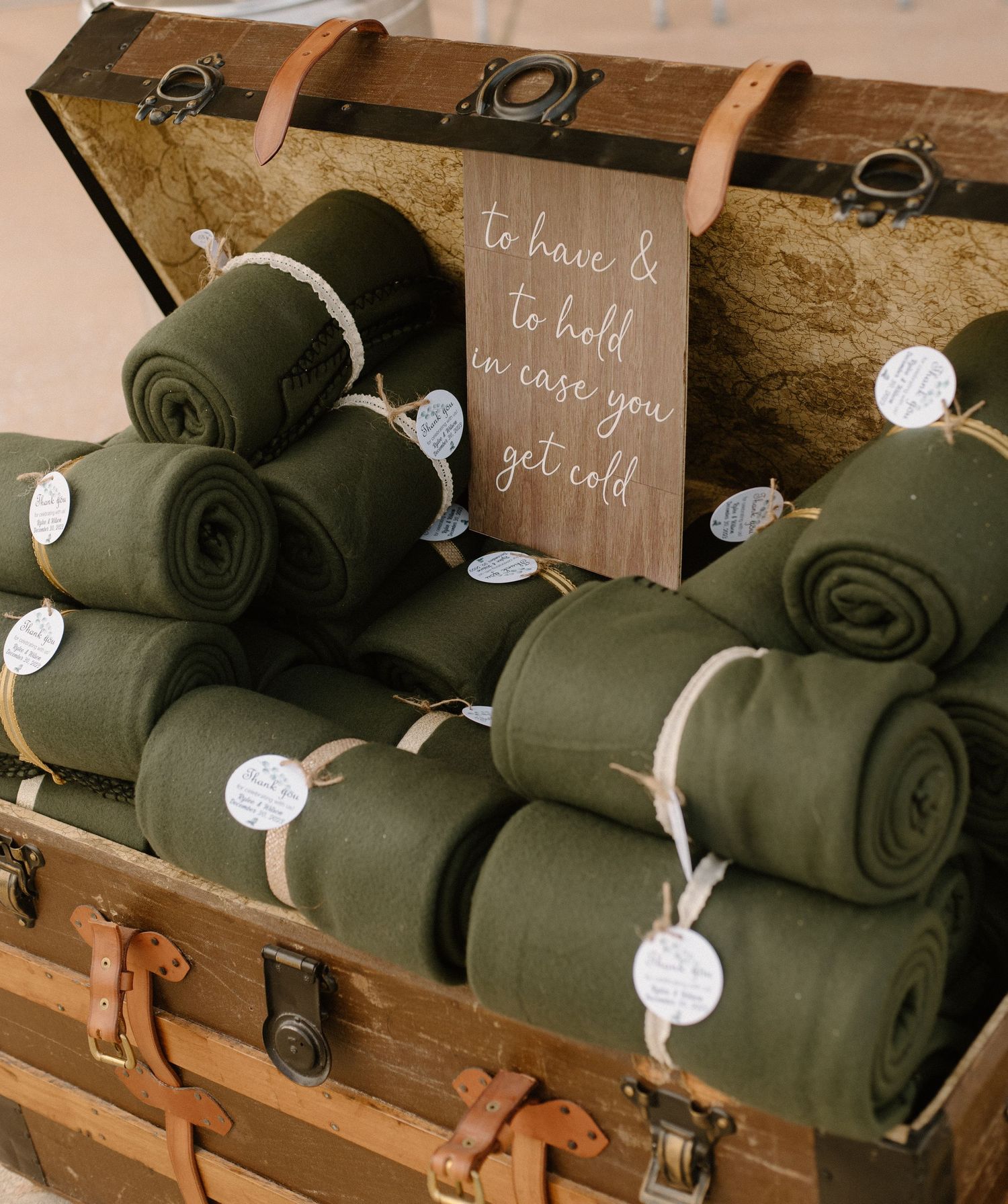 Vintage trunk filled with olive green blankets and a rustic wedding favor sign.