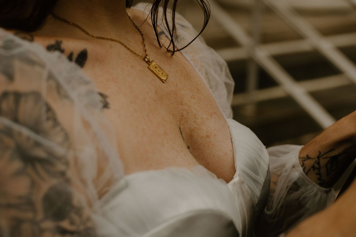 Close-up detail shot of a white wedding dress bodice with visible tattoos and a delicate necklace.